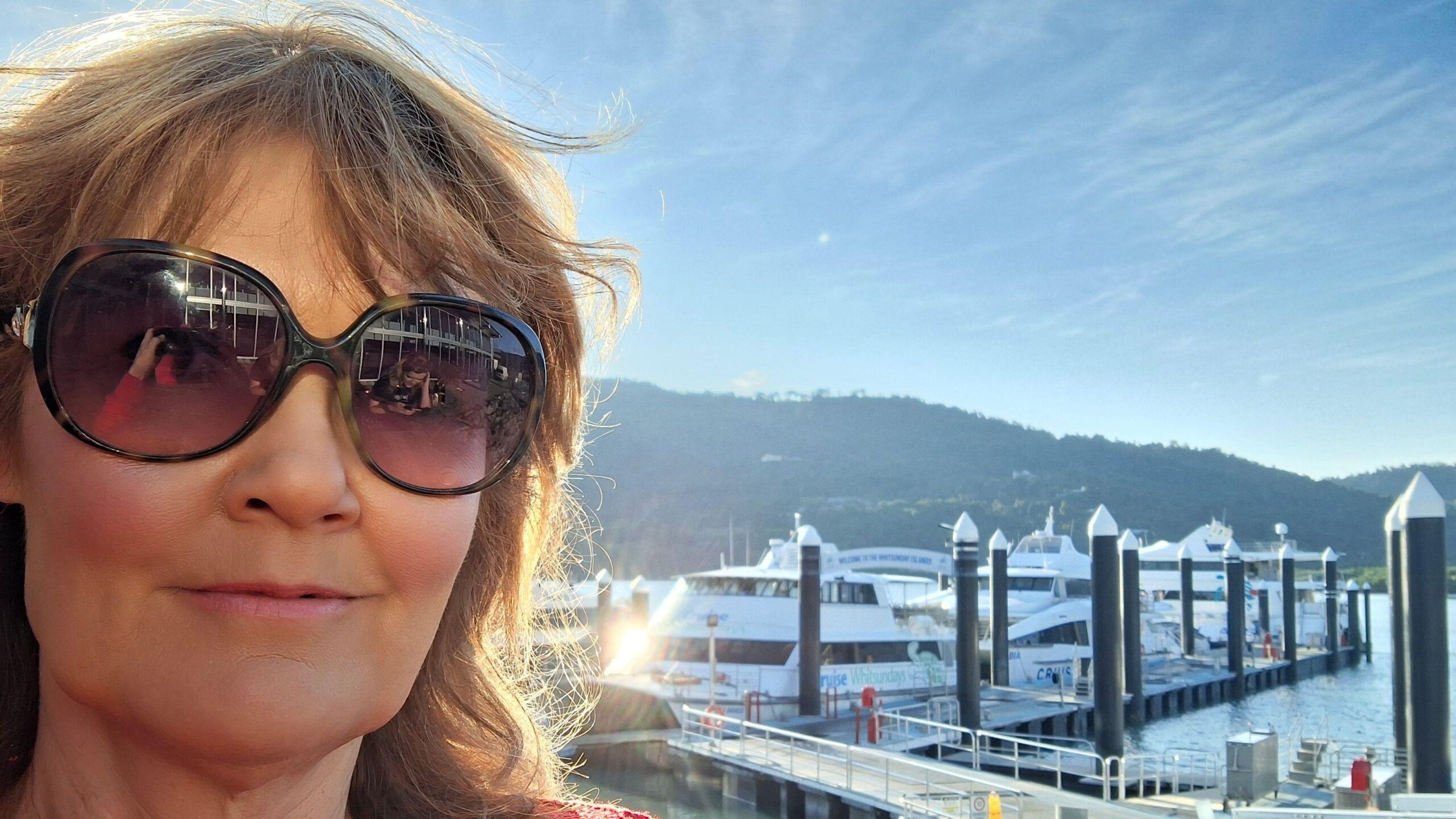 Karen Green lleva gafas de sol mientras está de pie frente a un puerto lleno de barcos.