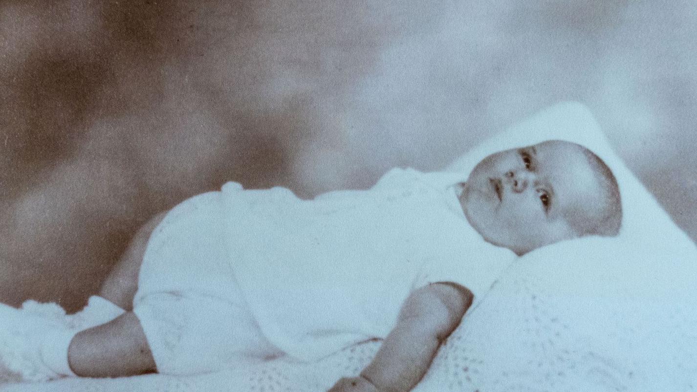 Una fotografía de un bebé vestido de blanco y acostado sobre una manta blanca.