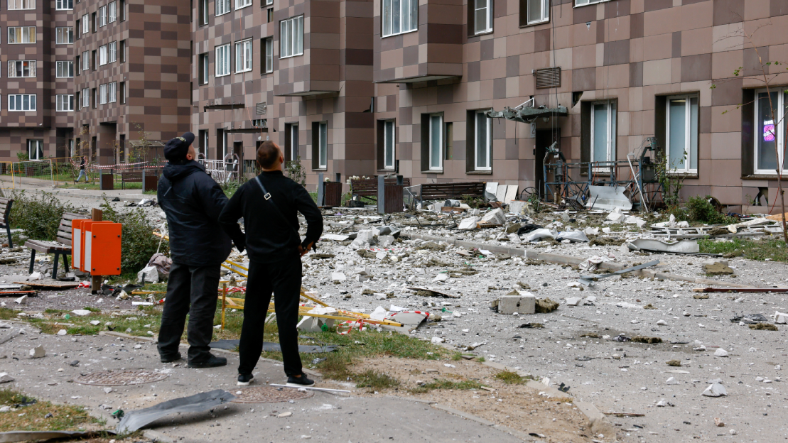 Dos policías vestidos de negro miran los escombros caídos de un edificio atacado.