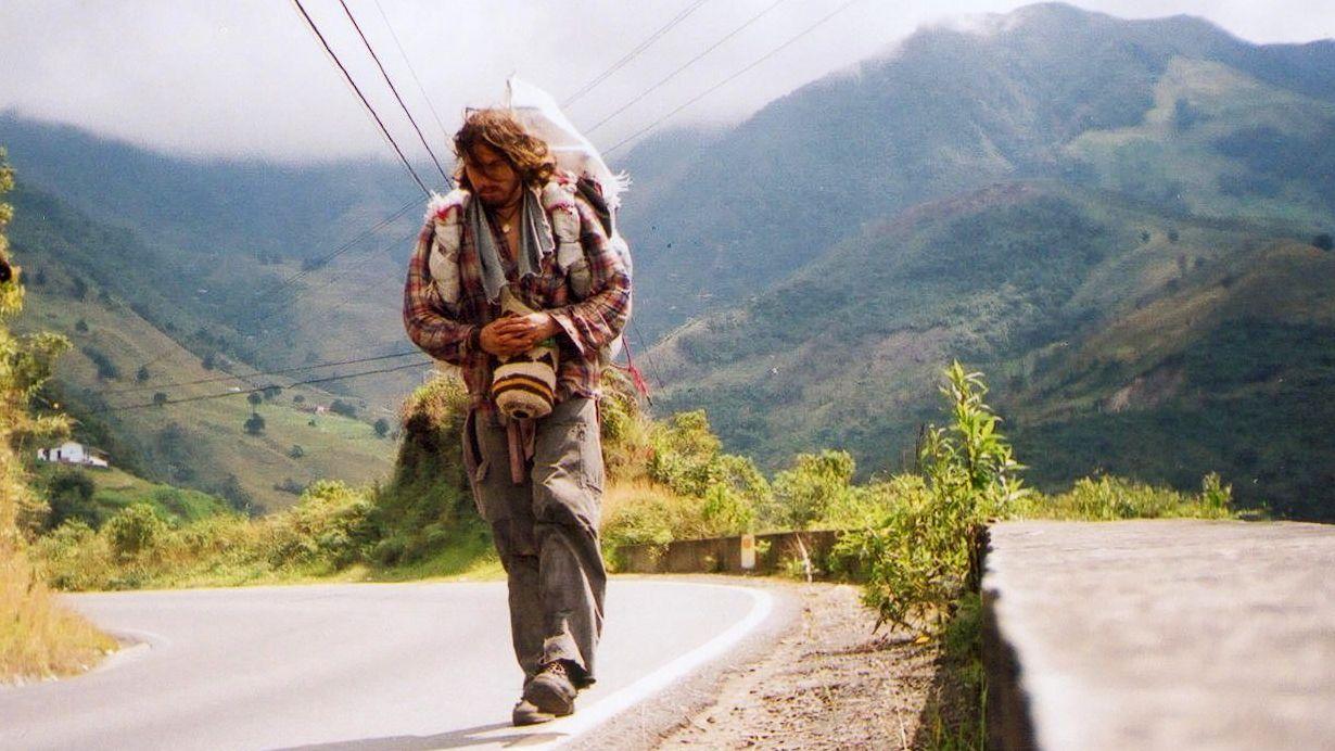 Un hombre con ropas andrajosas y cabello largo camina por un camino de montaña en Colombia.