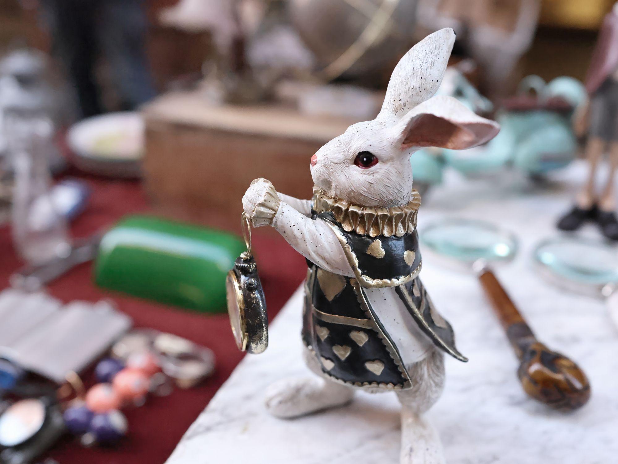 Una estatuilla de cerámica de un conejo blanco sosteniendo un reloj de bolsillo en las manos.