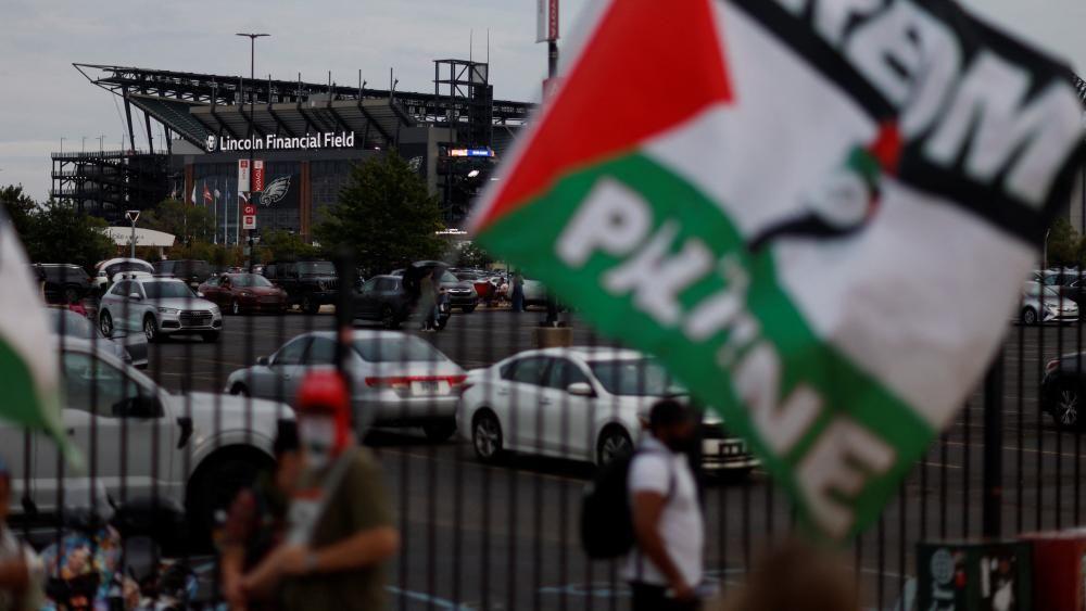 Unos cuantos manifestantes, uno de ellos ondeando una gran bandera con los colores palestinos blanco, negro, verde y rojo, se encuentran cerca de un aparcamiento junto al Lincoln Financial Field. 
