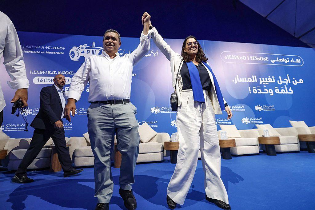 El Mansouri, de la mano de una compañera de PAM, durante uno de los mítines del partido. Viste un traje blanco y está de pie sobre una plataforma azul con el logotipo de PAM en varios idiomas.