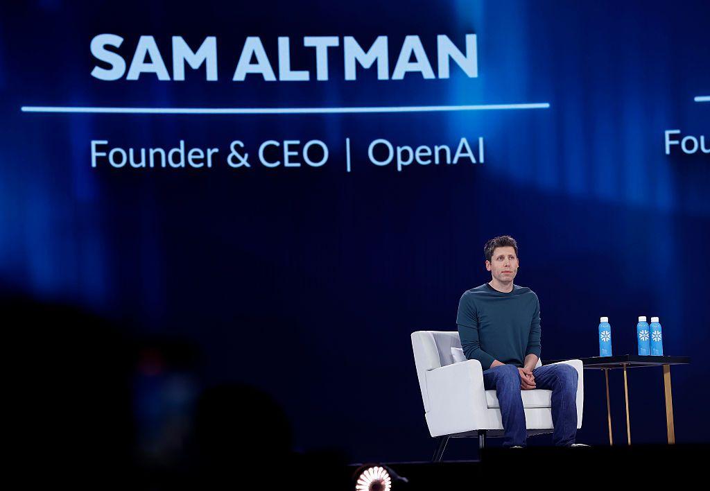 Sam Altman, sentado en un escenario en una silla blanca. Su nombre y cargo están proyectados detrás de él.
