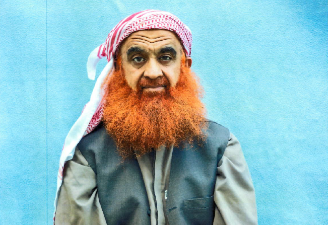 Una fotografía de Khalid Sheikh Mohammed difundida por su equipo legal. En ella aparece con una larga barba rojiza y un pañuelo blanco y rojo en la cabeza, además de una camisa gris y una chaqueta sin mangas de color gris oscuro.