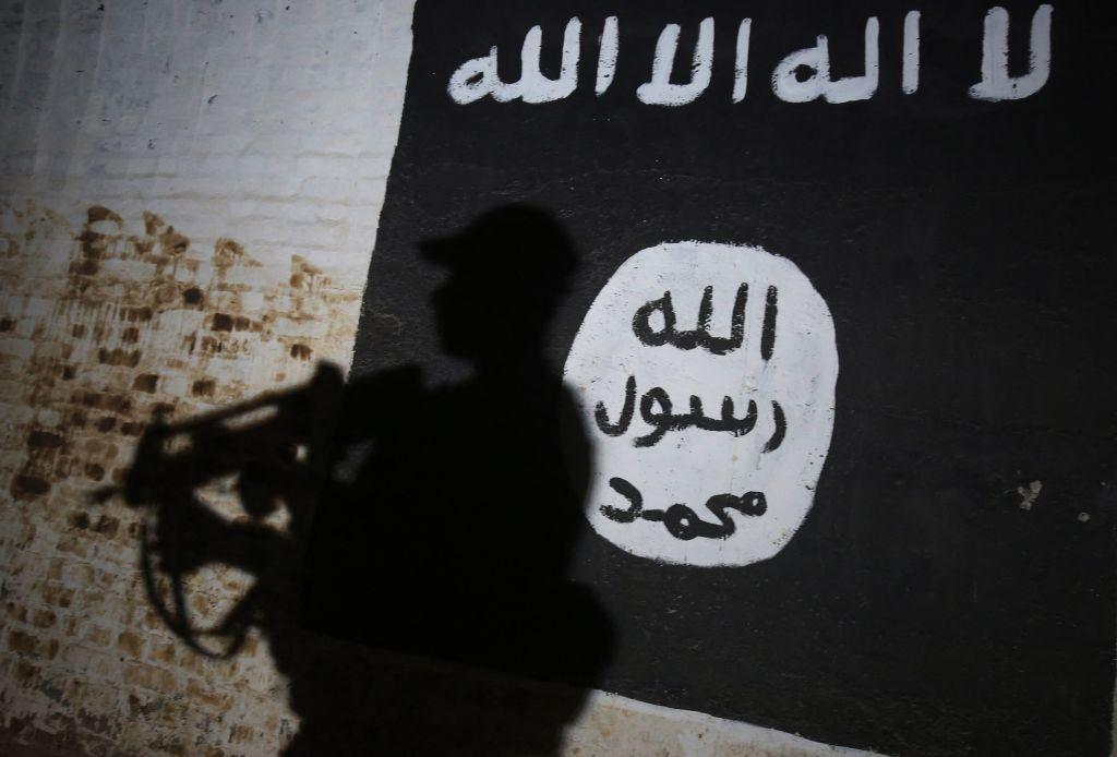 La sombra de un combatiente armado se proyecta sobre una pared pintada con la bandera del Estado Islámico (EI).