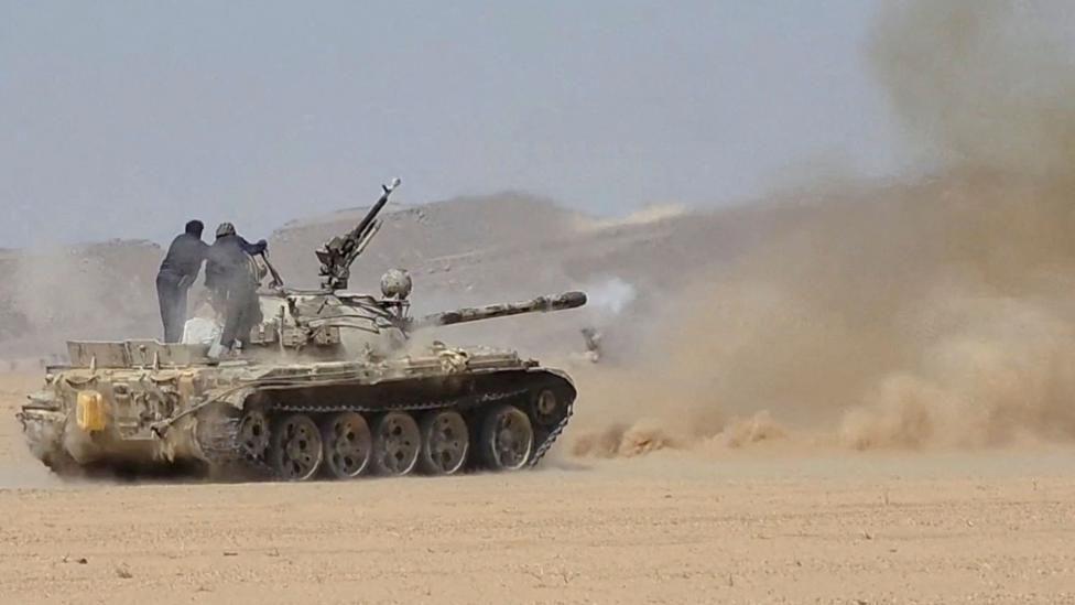 Un tanque de guerra disparando en medio de un desierto. 