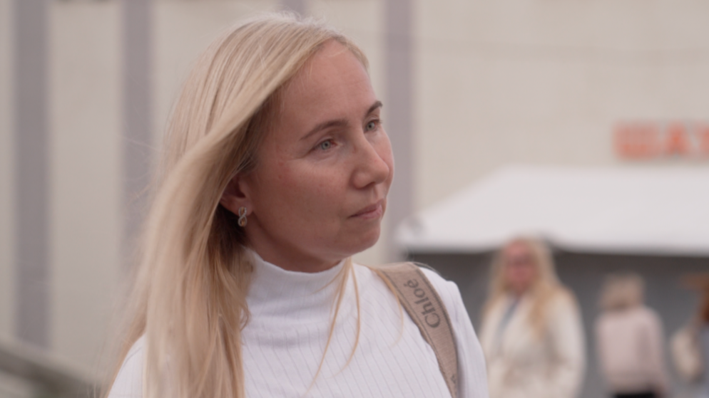 Olga luce una blusa blanca con la correa de un bolso Chloé visiblemente colgada al hombro. Tiene el pelo rubio y pendientes con forma de número 8.