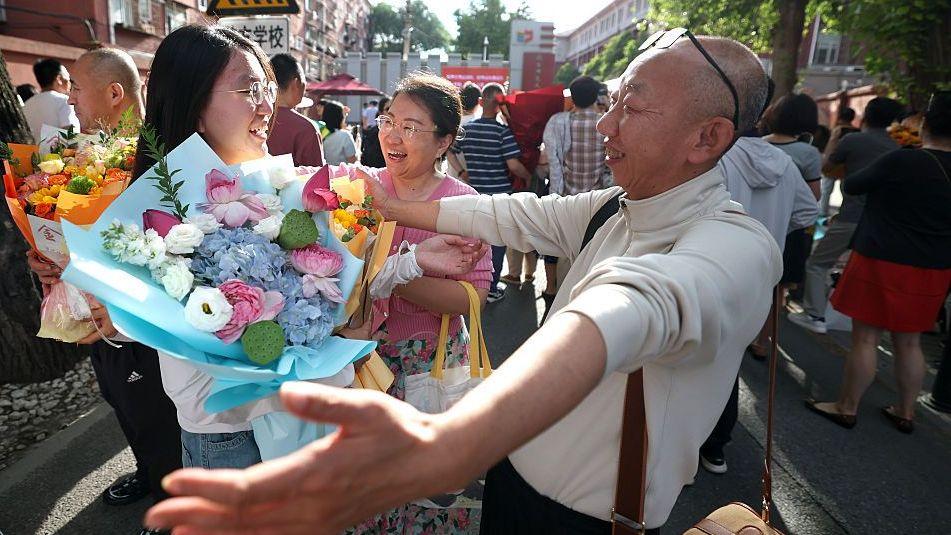 Un estudiante es abrazado por su padre a la salida del lugar del examen tras la Prueba Nacional de Ingreso a la Universidad de China 2026, el 10 de junio de 2026 en Pekín, China. Ella sonríe y sostiene un ramo de flores.