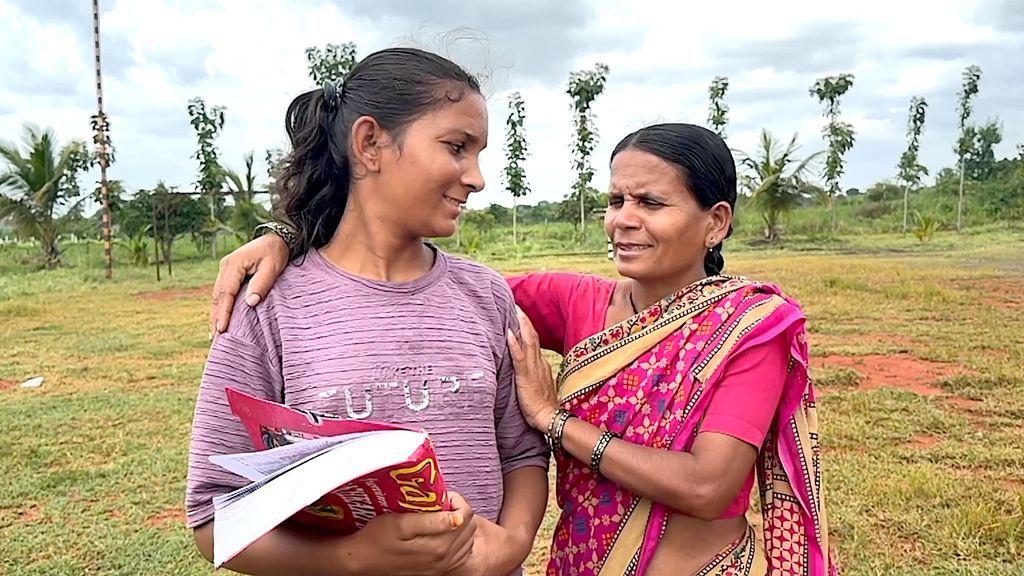 Con un libro de texto voluminoso en la mano, vestida con una blusa rosa a rayas y con el pelo largo recogido, Pooja, de 22 años, está de pie en el campo indio, sonriendo a su madre, Ramabai Ranveer, de 47 años, que lleva el mismo sari largo, vaporoso, colorido y estampado con el que corrió la carrera popular de 3 km de Amrit Daud, y que la abraza.