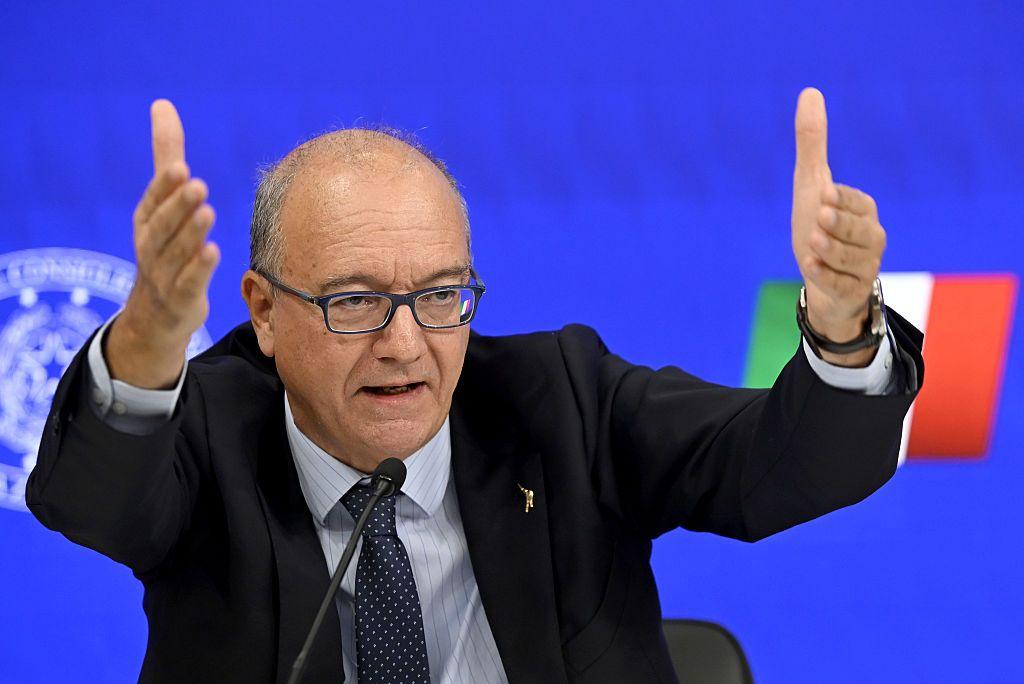 Ministro de Educación y Mérito de Itaia, Giuseppe Valditara, con los brazos en alto durante una intervención. Viste traje oscuro y corbata, y en el fondo se ve una pequeña bandera italiana.