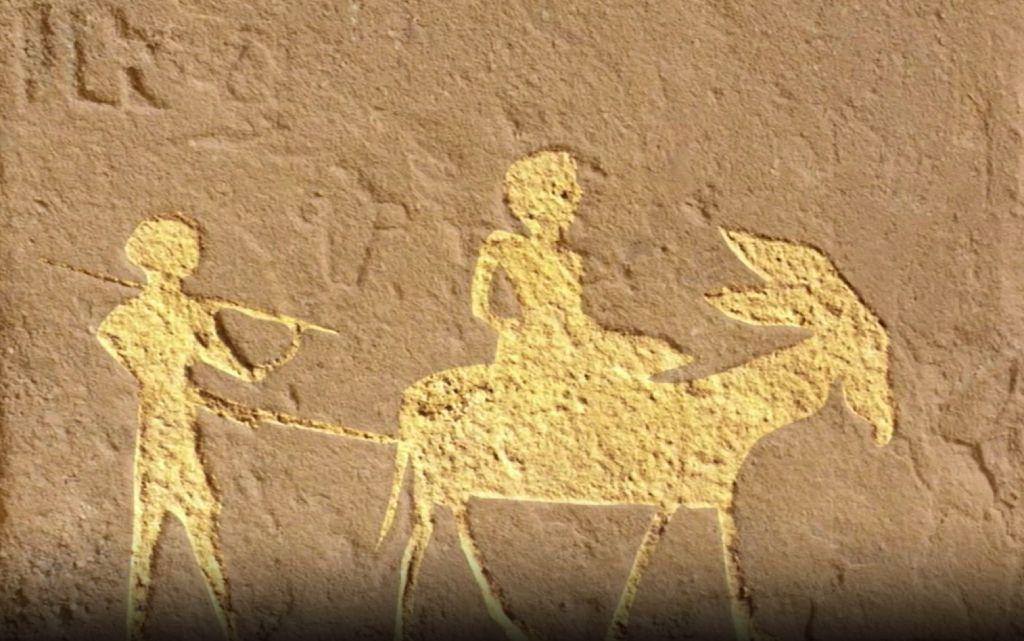 Tallado en piedra, un hombre sobre un burro y otro guiándolo