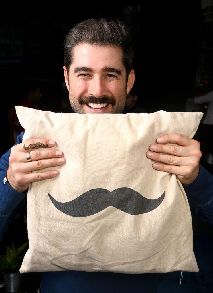 Un hombre sonriendo con un cojín en el que está dibujado un mostacho.