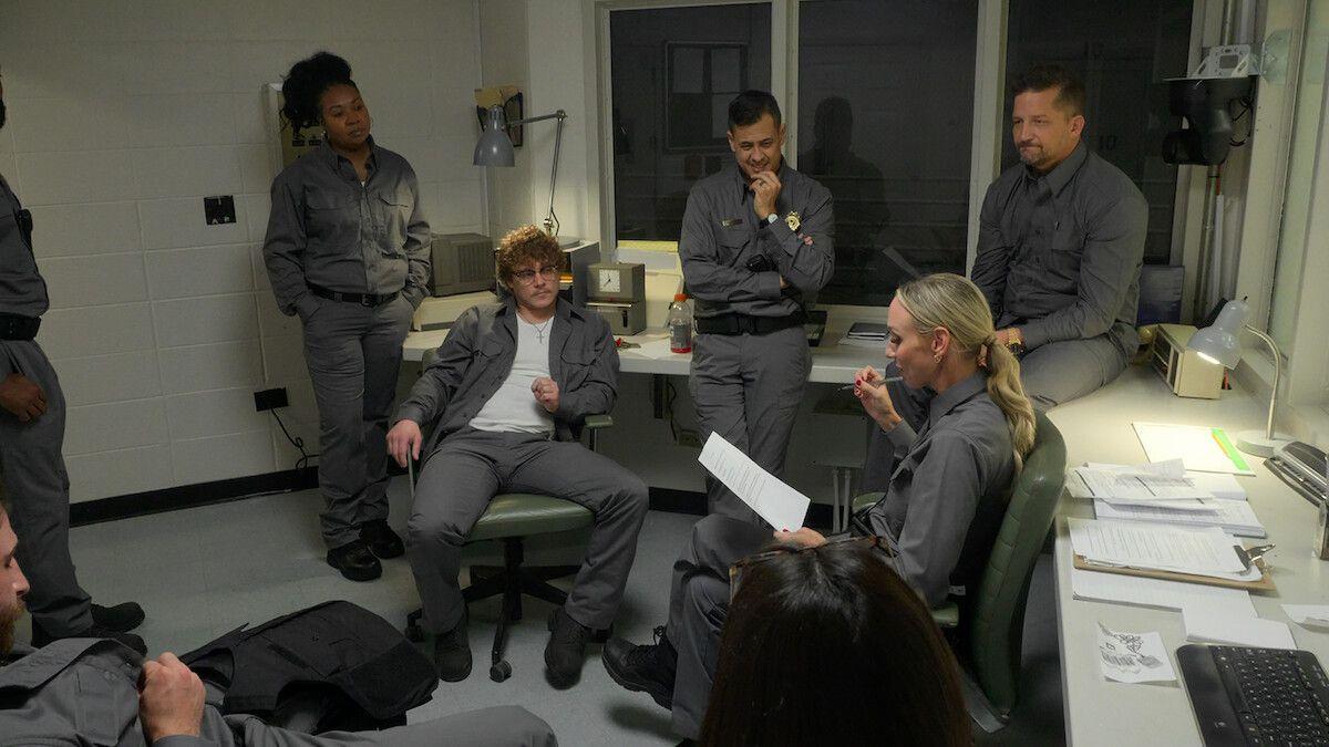 En la serie de telerrealidad de Netflix "El experimento de la cárcel de Stanford: un nuevo enfoque", siete participantes vestidos con uniformes grises permanecen sentados y de pie en una sala de control durante una reunión.