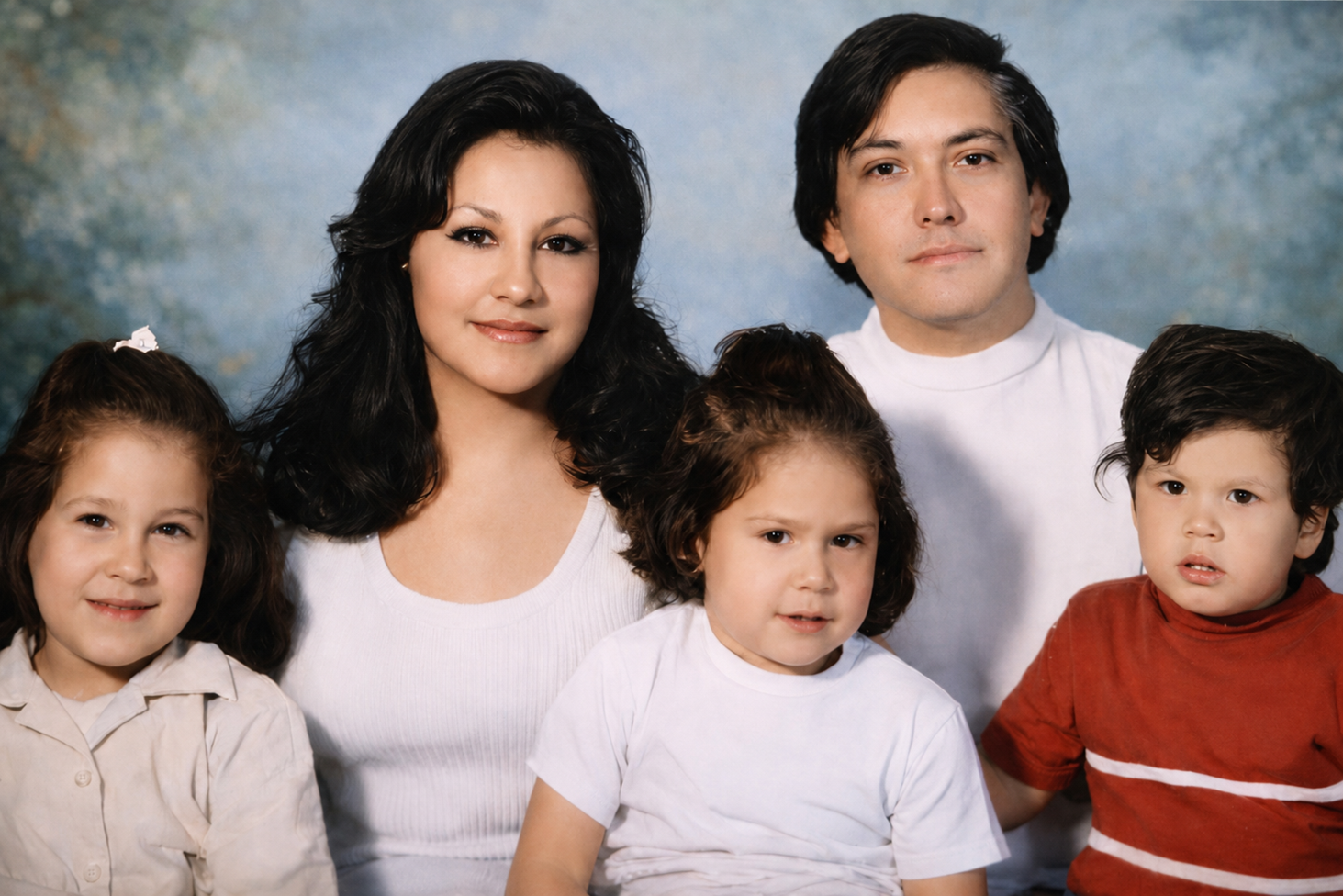 Eugenia y Rodolfo, vestidos con camisas blancas. En sus piernas tienen a sus hijos: Jenny, que tiene una camisa beige, Chelo, una camisa blanca, y Rudy, con una camisa roja.