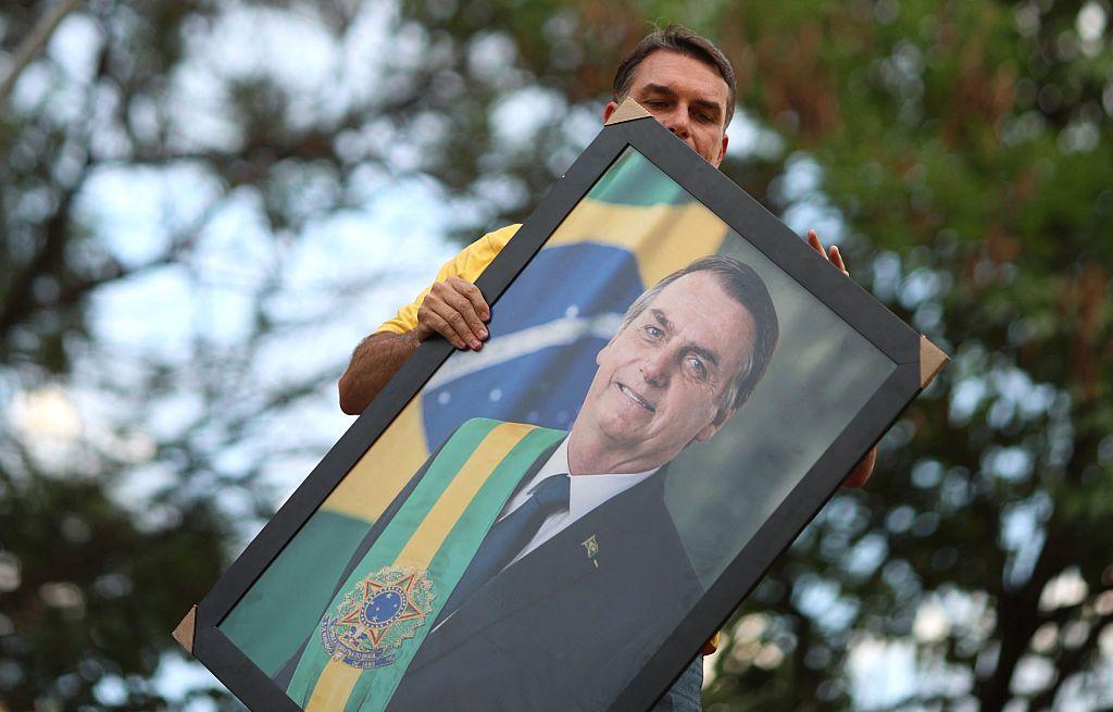 Flávio Bolsonaro sujeta un retrato de su padre, Jair Bolsonaro, con la banda presidencial de Brasil. 