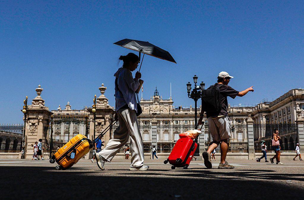 Unos turistas ante el Palacio Real de Madrid con sus maletas.