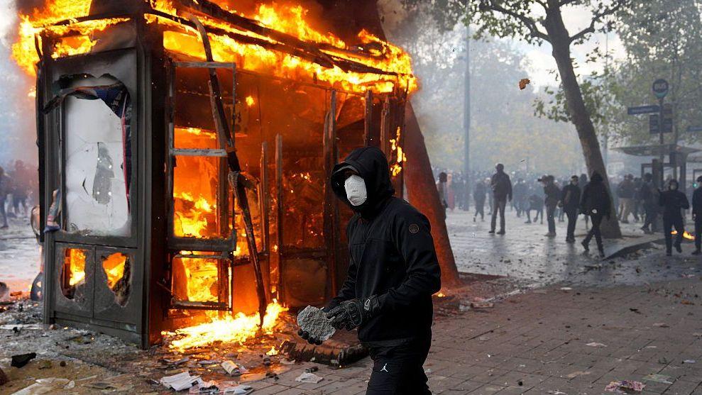 Un manifestante sostiene una piedra mientras un quiosco arde durante una protesta cerca de la Plaza de la República en París, Francia. Foto: 17 de octubre de 2026