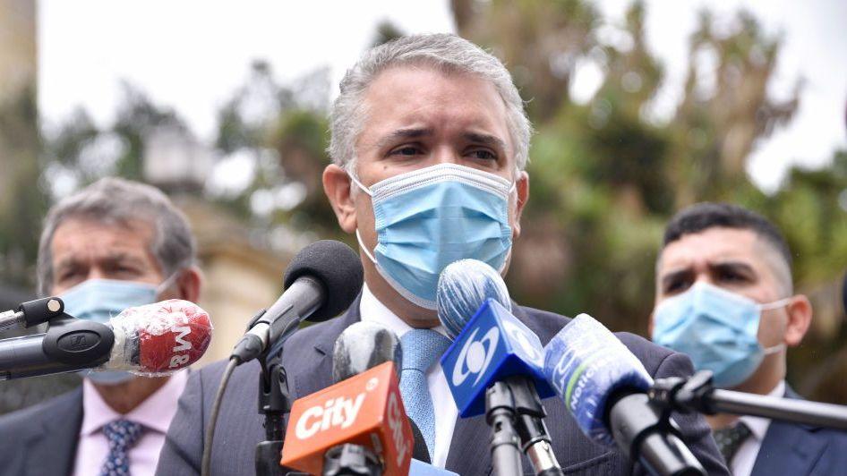 El entonces presidente Iván Duque usando un tapabocas mientras habla frente a micrófonos envueltos en plástico.