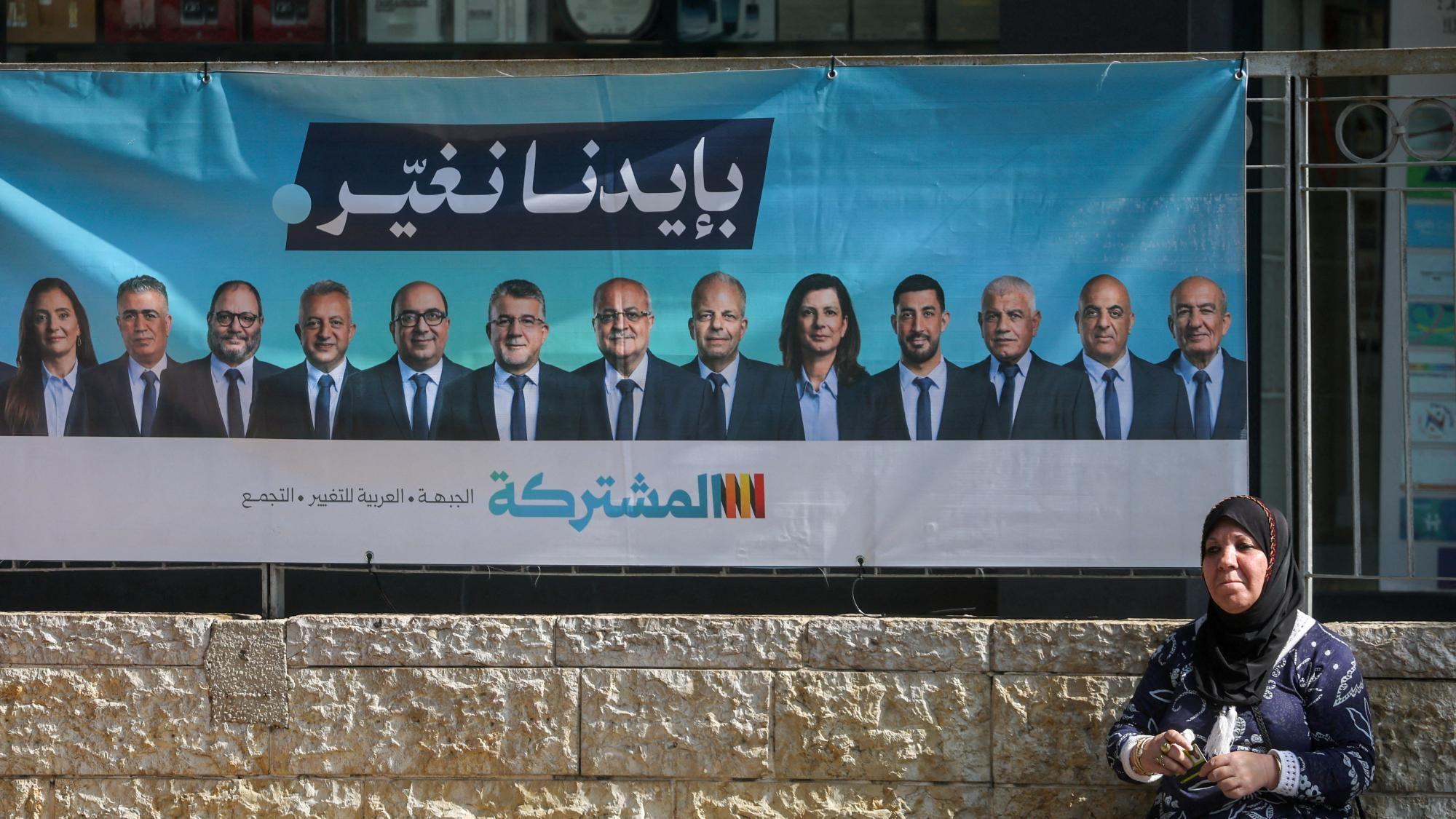 Una mujer se sienta cerca de una pancarta de campaña electoral con los líderes de la Lista Conjunta, en Nazaret, Israel (10 de octubre de 2026).