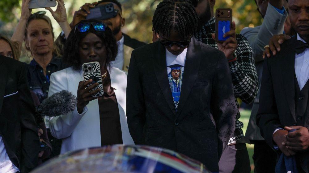 Un amigo de Pierre Damas Bel llora en el funeral. Lleva una camiseta con su imagen.