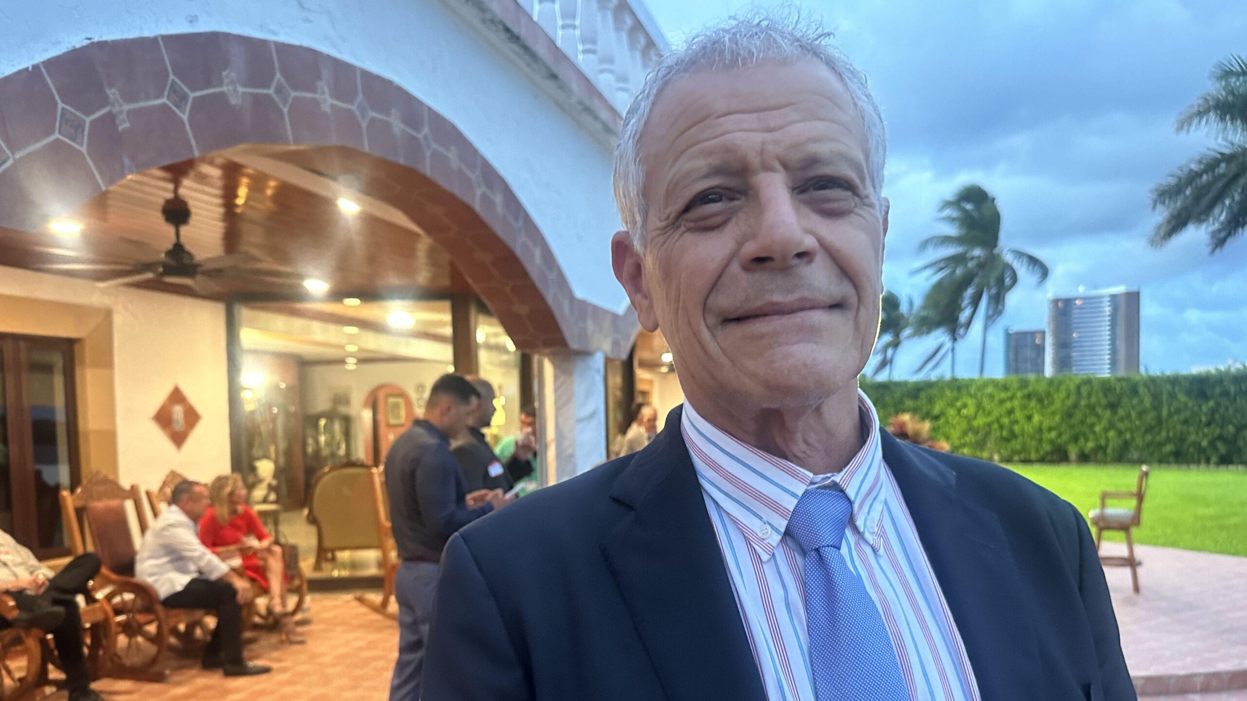 Hugo Orizondo sonríe a la cámara, de pie frente a otros invitados en el evento en Miami.