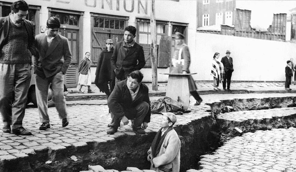 Residentes de Valdivia en 1960 después del terremoto. Un hombre está parado dentro de una fractura en la calle tan profunda que le llega hasta el cuello.