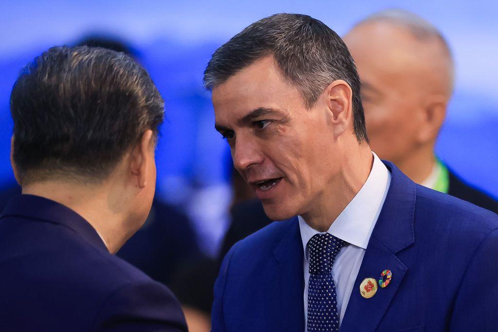 Xi Jinping escucha al presidente español, Pedro Sánchez, que sale de frente con traje y corbata oscuros. Xi está de espaldas. 