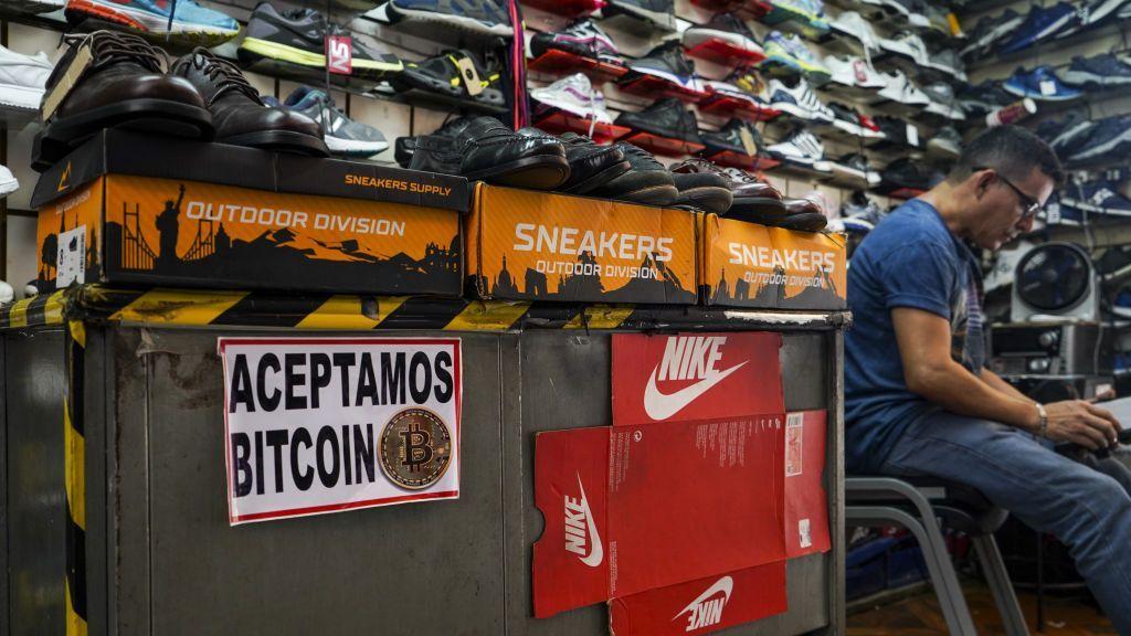 Un hombre espera a los clientes en una tienda de zapatos con un letrero que muestra la aceptación de Bitcoin como método de pago el 15 de junio de 2022 en San Salvador, El Salvador. (Foto de Camilo Freedman/NurPhoto vía Getty Images)