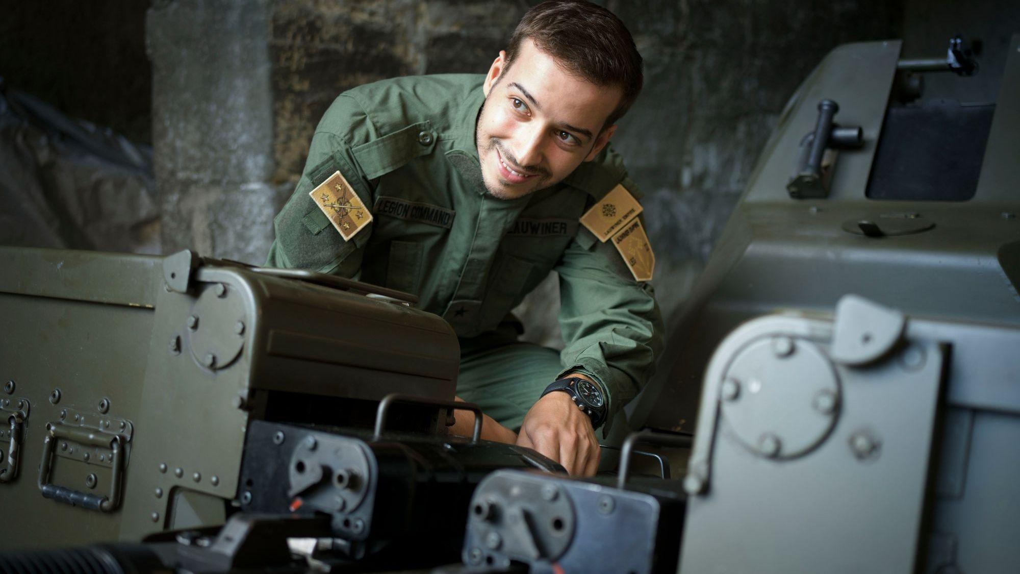 Lauwiner, vestido con un uniforme militar verde, sonríe a la cámara mientras está en cuclillas.
