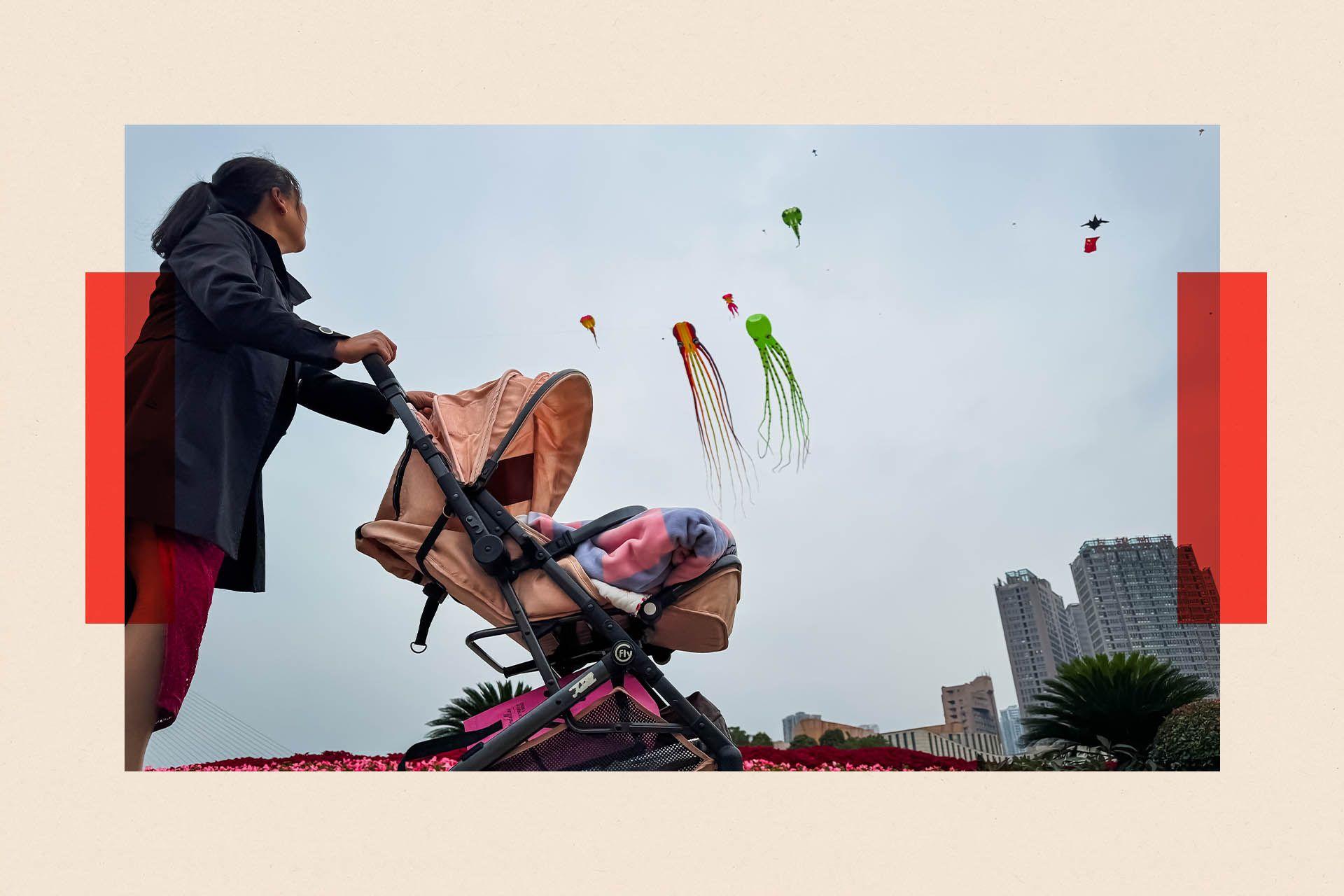 Una mujer empuja un cochecito rosa cerca del horizonte de la ciudad. Dos cometas vuelan en el cielo.