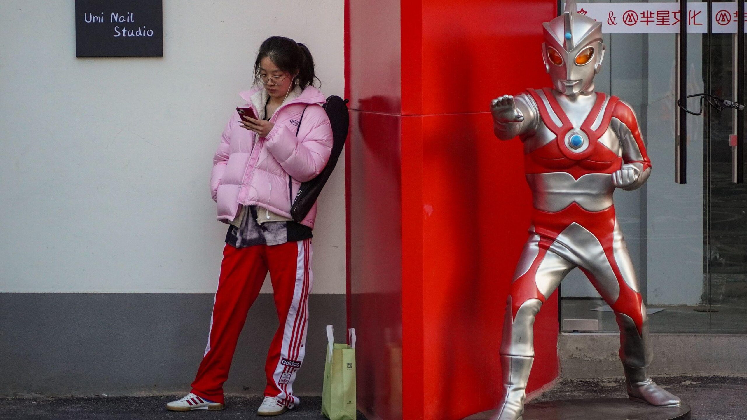 Una joven se encuentra de pie junto a una estatua de Ultraman de tamaño natural frente a una tienda.