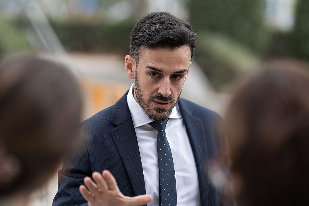 El abogado Aitor Martínez, con traje y corbata oscuros, alza la mano derecha hasta la altura de su pecho a su llegada a la Audiencia Nacional para la primera audiencia del proceso de extradición. 