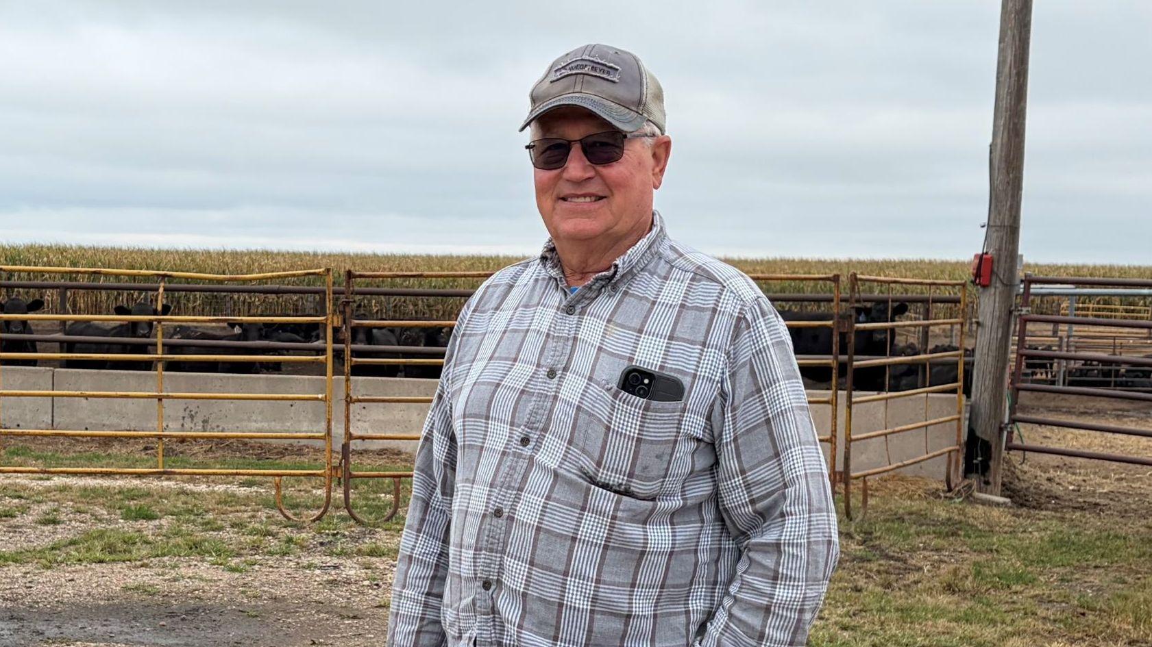 Don Cantrell lleva una camisa a cuadros y una gorra y está de pie frente a una cerca de la granja.