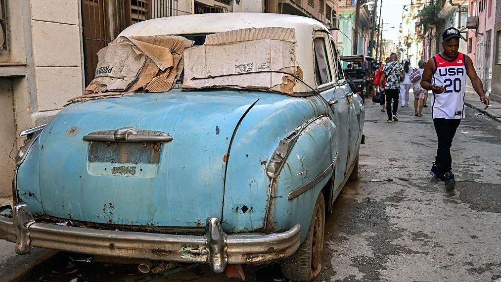 Un hombre pasa junto a un auto viejo en una calle del centro de La Habana.