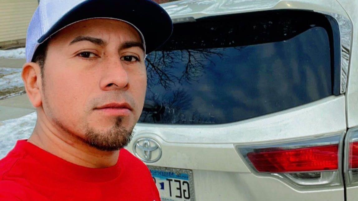 Kenis López en una selfie con una gorra y una sudadera roja, posa frente a un auto marca Toyota, frente a un fondo nevado.