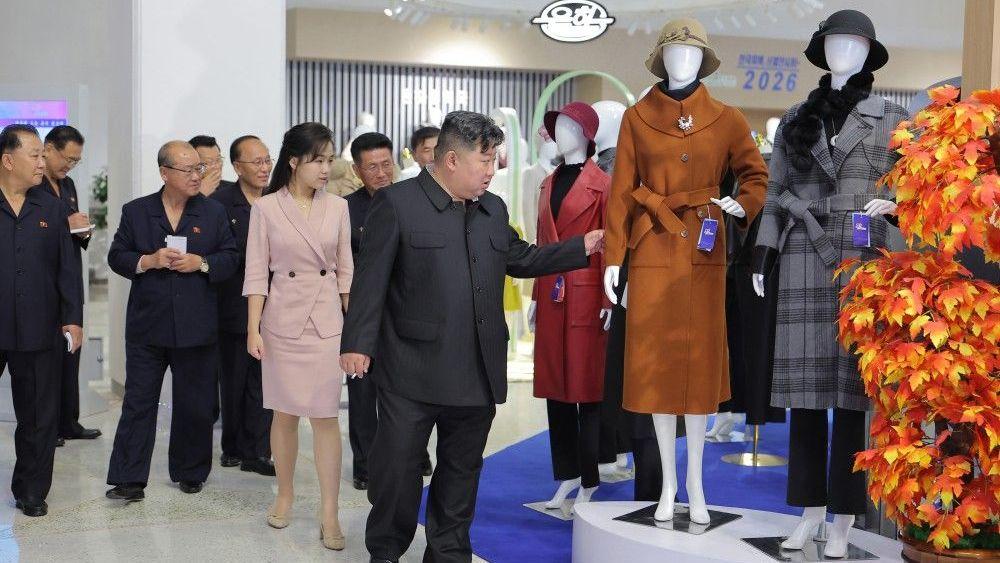 Kim Jong Un y su hija Kim Ju Ae observan un maniquí con un abrigo mientras un séquito de funcionarios los mira. 