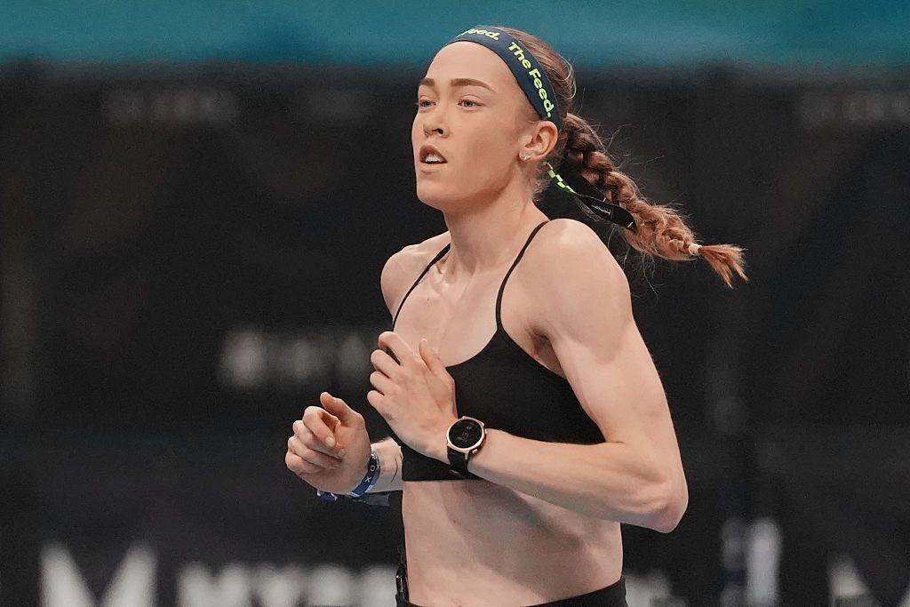 Joanna Wietrzyk lleva un sujetador deportivo negro y una diadema oscura con la leyenda "the feed" impresa en letras verdes. Tiene el pelo recogido en una trenza y está corriendo.