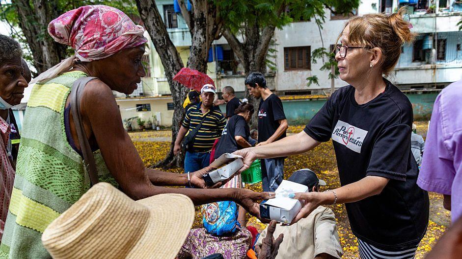 Una voluntaria de una iglesia distribuye cajas de alimentos de ayuda humanitaria a residentes en un parque público de La Habana.