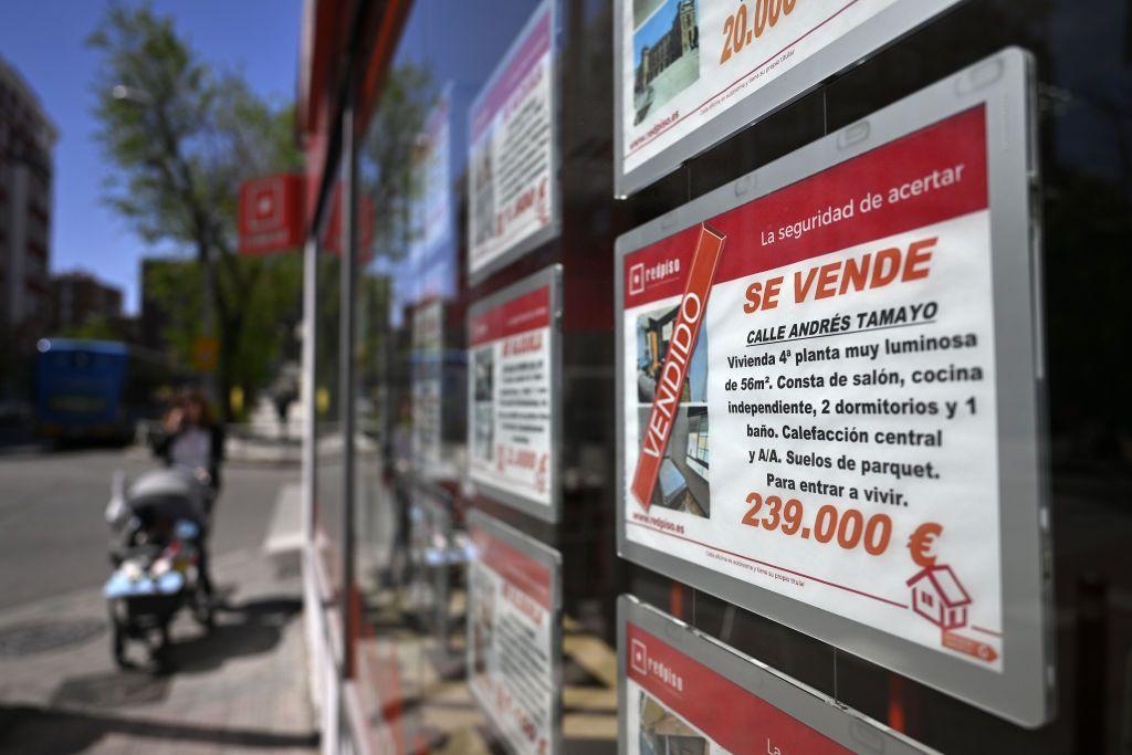 Un mujer empuja el coche de su bebé cerca de una vitrina de una agencia inmobiliaria en la que se vende carteles de vendido