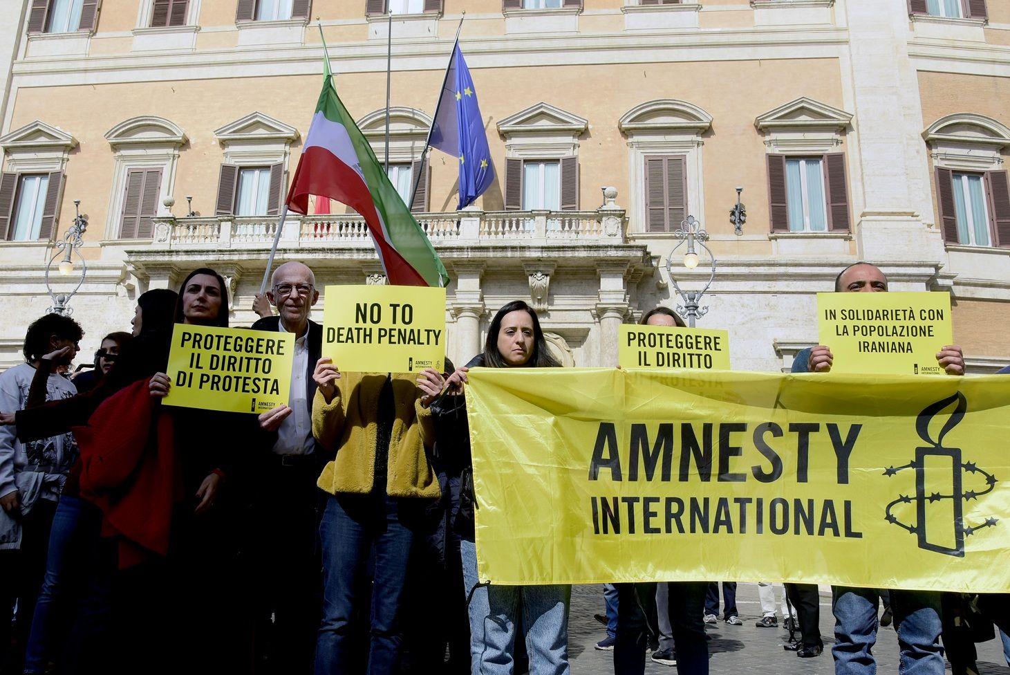 Un grupo de manifestantes con pancartas amarillas que, entre varias, dicen "No a la pena de muerte", "En solidaridad con el pueblo iraní", "Amnistía Internacional". Al fondo se ven las banderas de la Unión Europea y de Irán.

