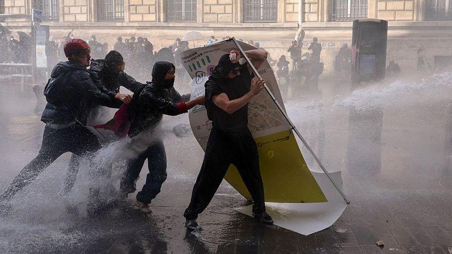 Manifestantes se protegen de un chorro de agua lanzado por la policía durante las protestas en París. 