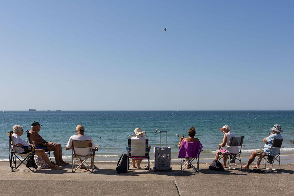 Un grupo de siete personas mayores sentadas en sillas plegables individuales mirando al mar en una Saint-Malo, en la Bretaña, Francia. 