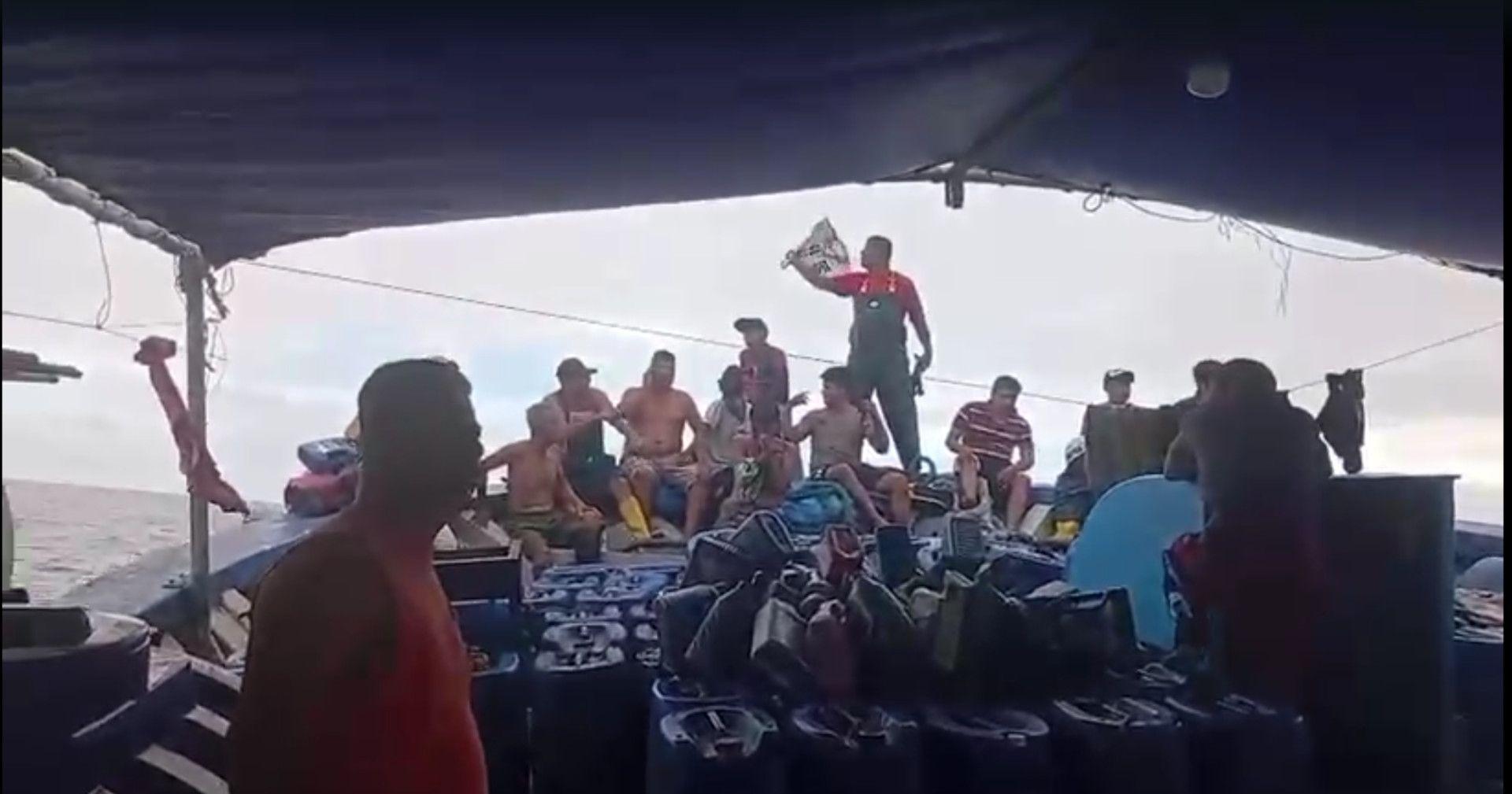 Un grupo de hombres están sentados en lo que parece ser la proa de un barco. Algunos no llevan camisetas.