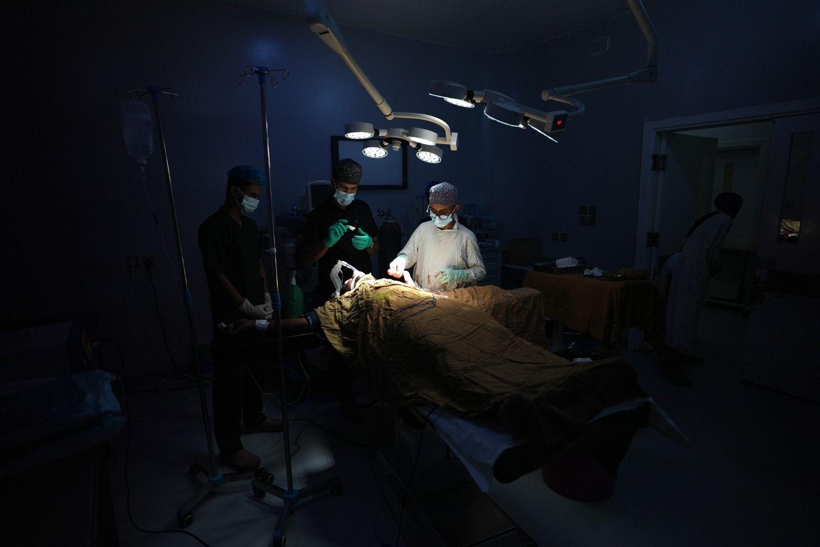 Personal médico rodea a un paciente en un quirófano de un hospital militar iluminado únicamente por luces portátiles.