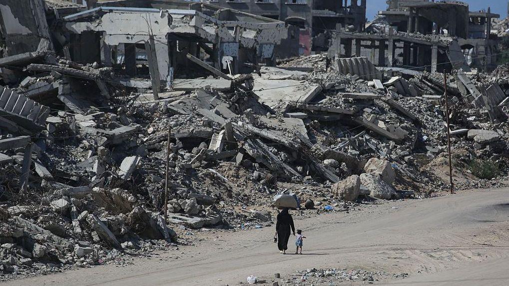 Una mujer y un niño caminan por un camino de tierra en medio de extensos daños en edificios y grandes escombros en Khan Younis, en la Franja de Gaza.