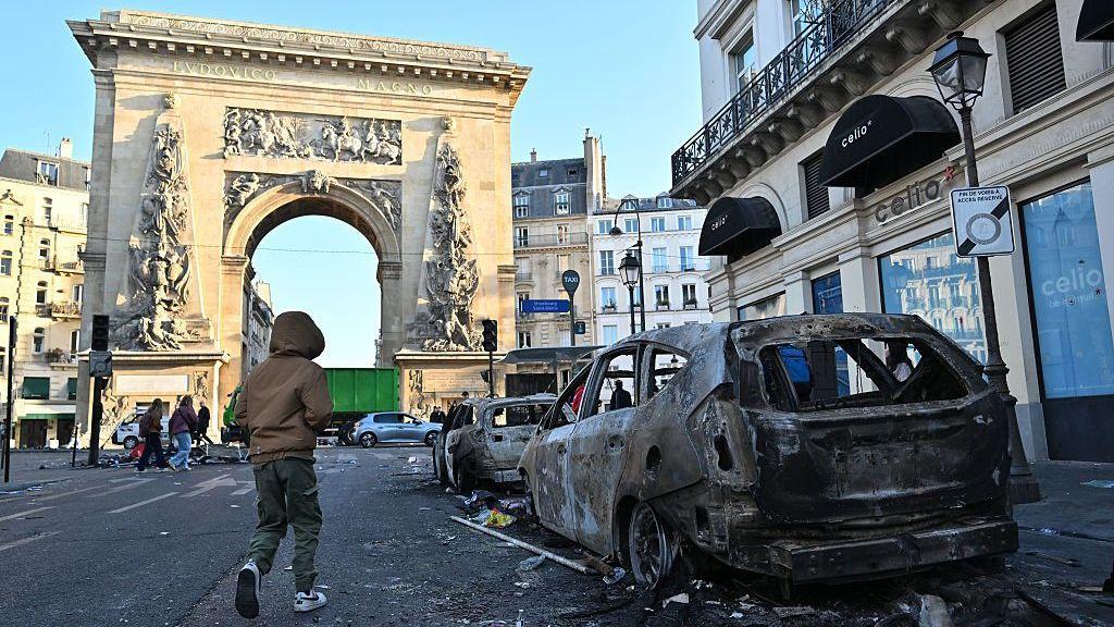 Una persona pasa junto a vehículos calcinados en París tras los enfrentamientos en las protestas.