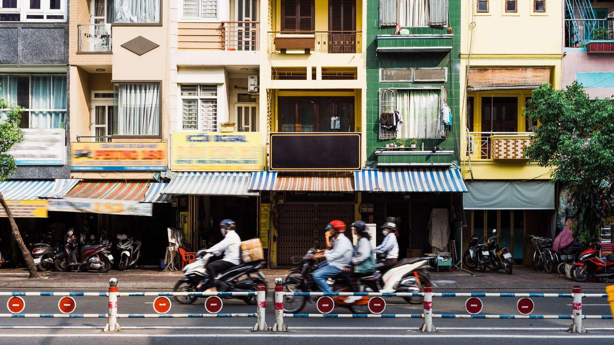Una calle de Ciudad Ho Chi Minh con pequeños edificios coloridos y motocicletas pasando por enfrente.