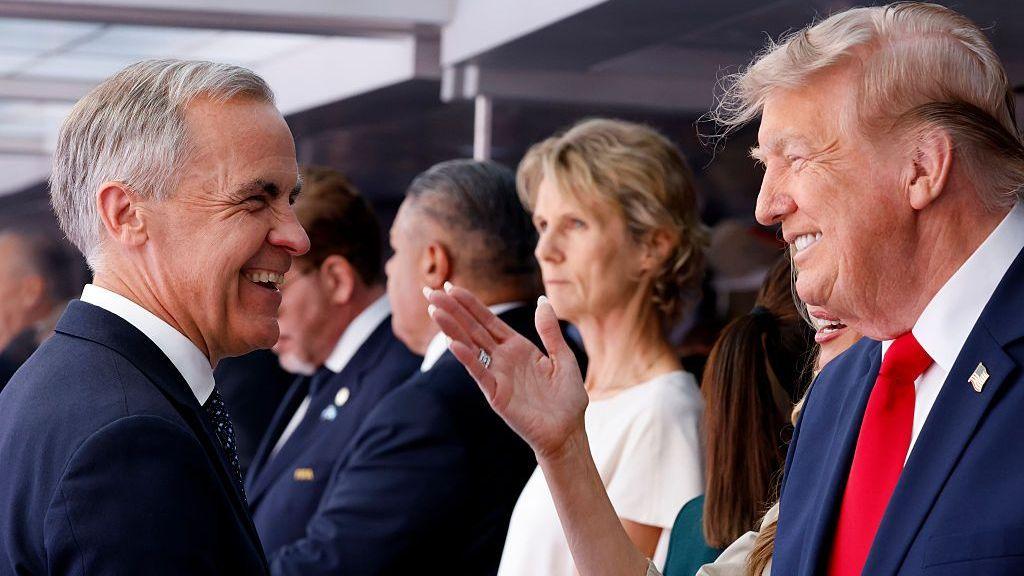 Mark Carney y Donald Trump, cada uno de perfil, comparten una sonrisa. Al fondo se puede ver una multitud. 