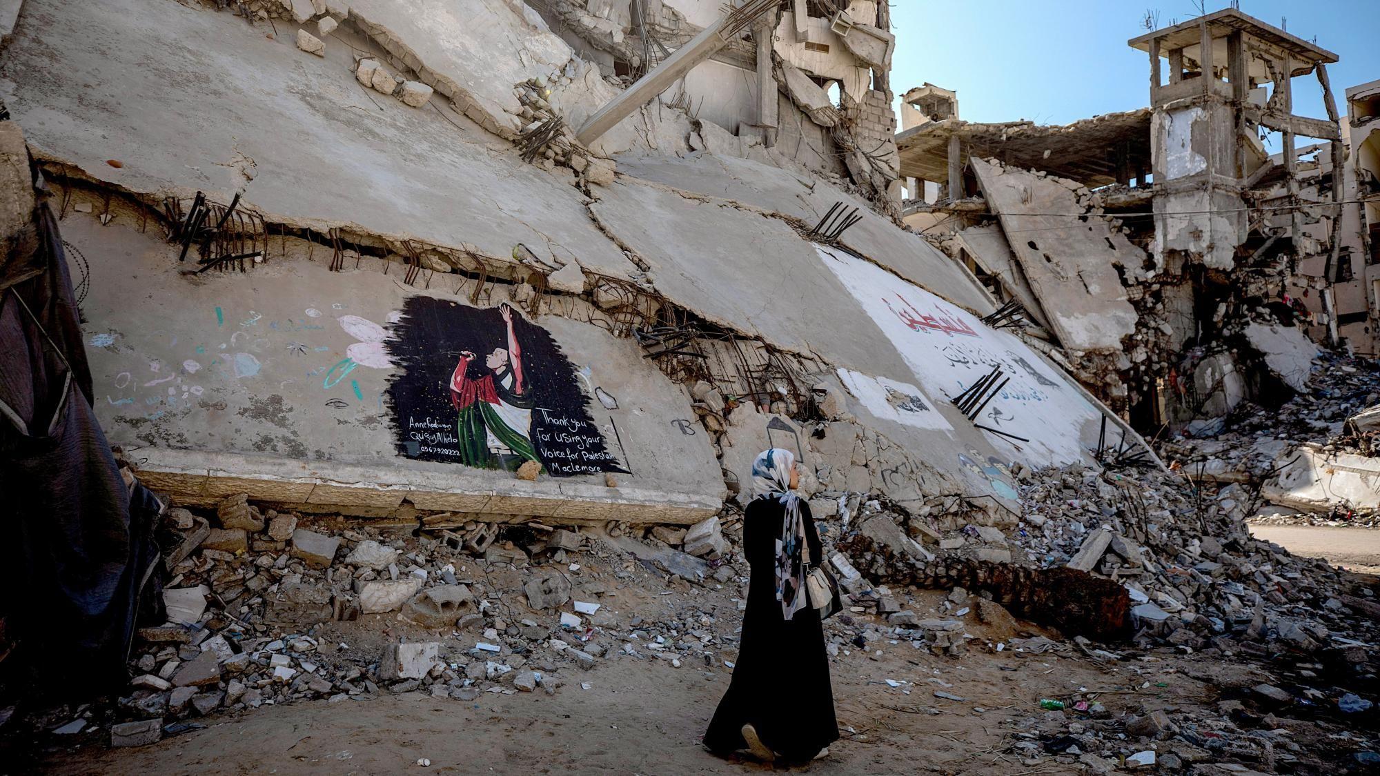 Una mujer pasa junto a un mural que representa al rapero estadounidense Macklemore en las ruinas de un edificio dañado por la guerra en la ciudad de Gaza (19 de septiembre de 2026).